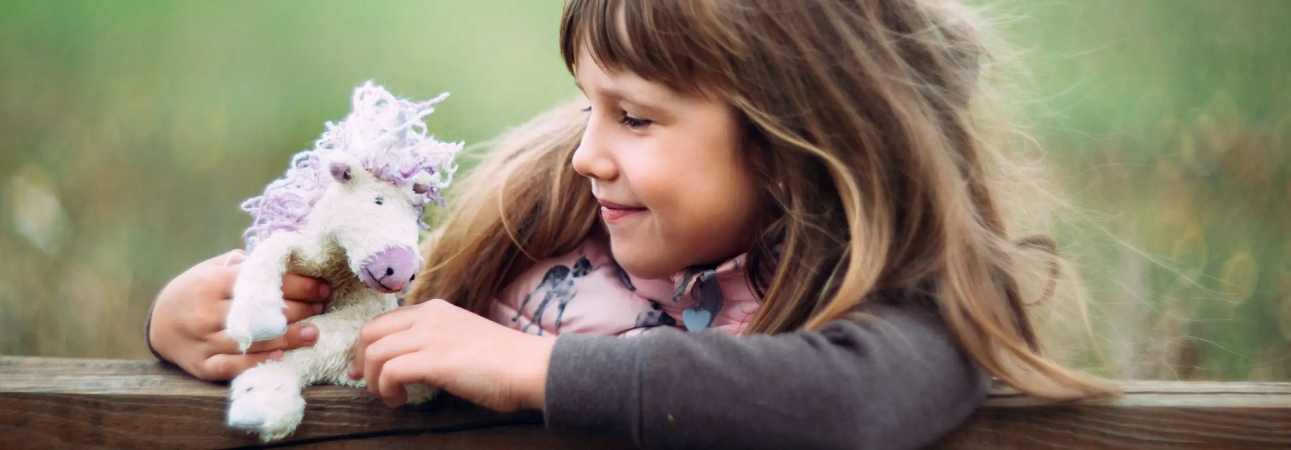 A young girl smiling while holding a soft unicorn toy